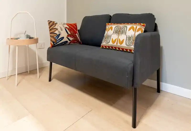 Un divanetto moderno compatto con cuscini fantasia posizionato contro una parete neutra, perfetto per un angolo conversazione accogliente.
