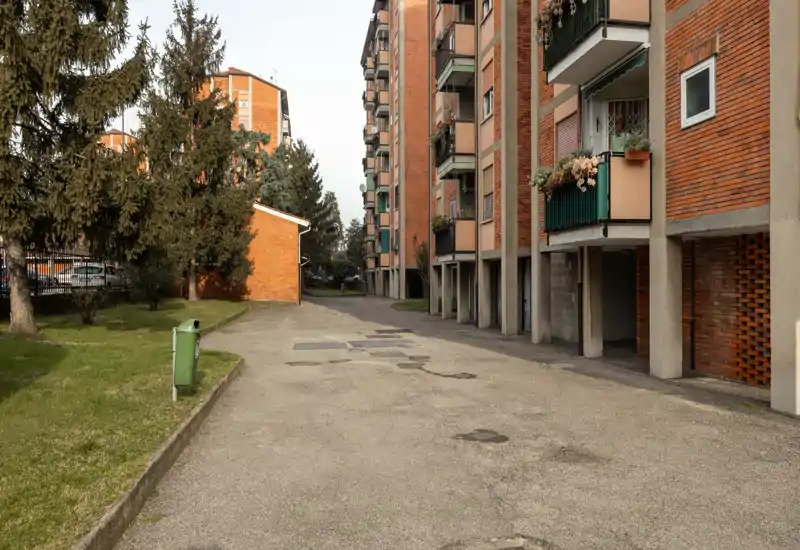 Cortile tra condomini in mattoni con corsia asfaltata, piccolo prato e alberi — uno spazio esterno condominiale tranquillo.