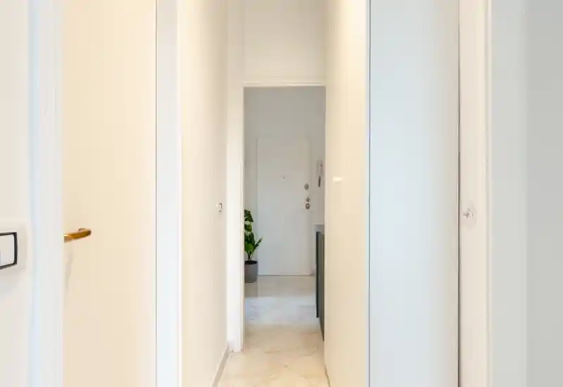 Ingresso luminoso e minimale con pavimento piastrellato, porta d'ingresso visibile e una piccola pianta in vaso — sensazione pulita e accogliente.