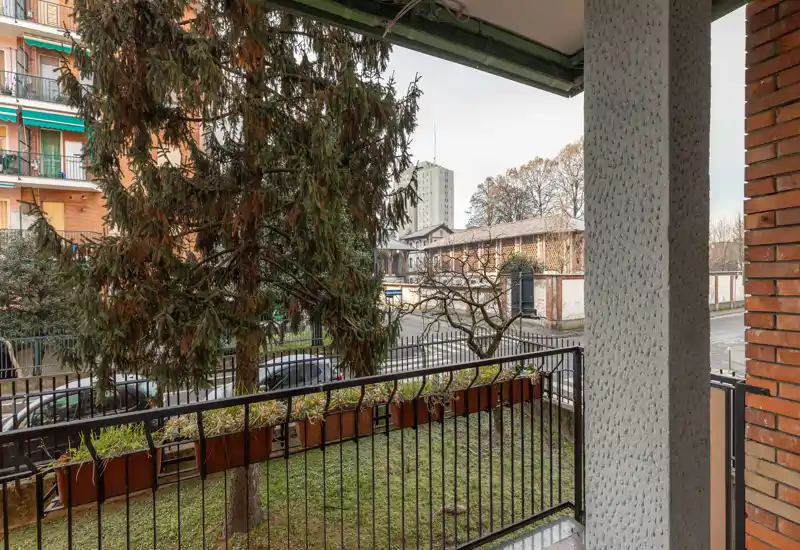 Balcone a piano terra con ringhiera in metallo e fioriere che si affaccia su una strada tranquilla e alberi maturi; ideale per un piccolo angolo esterno.