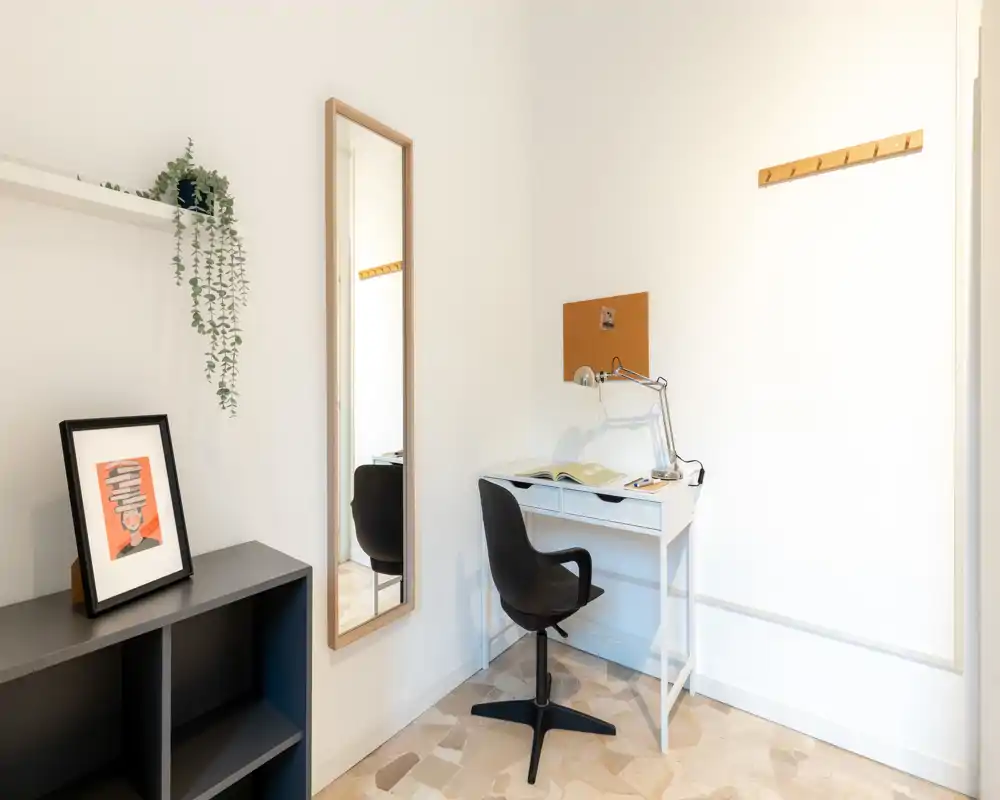 Coin bureau lumineux et minimaliste dans l'espace de vie : petit bureau blanc avec lampe de travail, chaise pivotante noire, miroir pleine longueur et décorations simples pour un espace de travail fonctionnel et soigné.