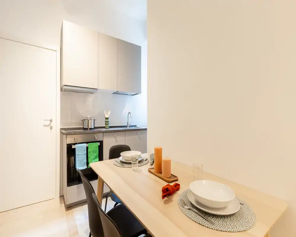 Cocina moderna y compacta con horno y fregadero integrados, junto a una pequeña mesa de comedor de madera puesta con velas y manteles individuales.