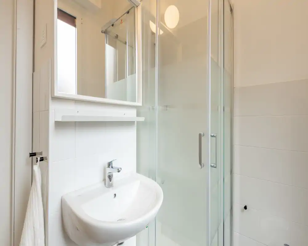 Baño moderno y luminoso con lavabo mural, espejo/armario y cabina de ducha de vidrio con paneles esmerilados.