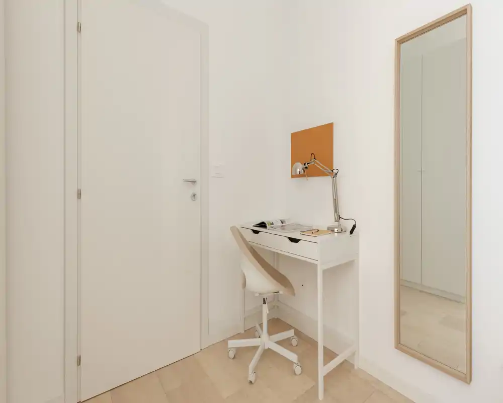 Piccolo ingresso luminoso con una scrivania compatta e sedia girevole; arredi neutri e uno specchio a figura intera creano un ingresso ordinato e funzionale.