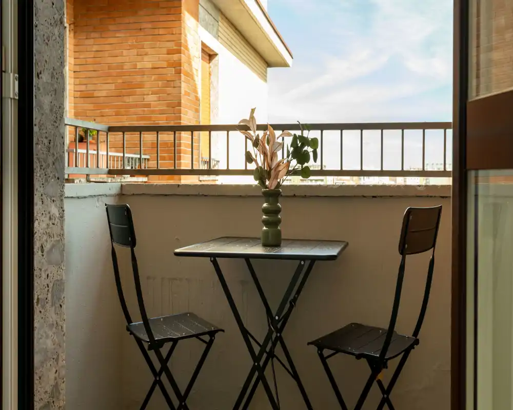 Piccolo balcone accogliente con tavolino bistro, due sedie pieghevoli e un vaso decorativo — perfetto per un caffè mattutino con vista sulla città.