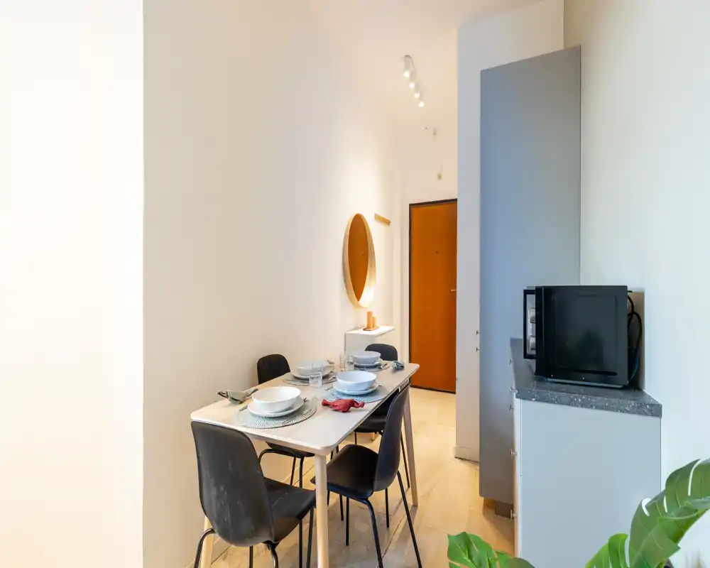 Accogliente zona pranzo stretta con tavolo apparecchiato per quattro, sedie moderne e luce calda — perfetta per appartamenti compatti.