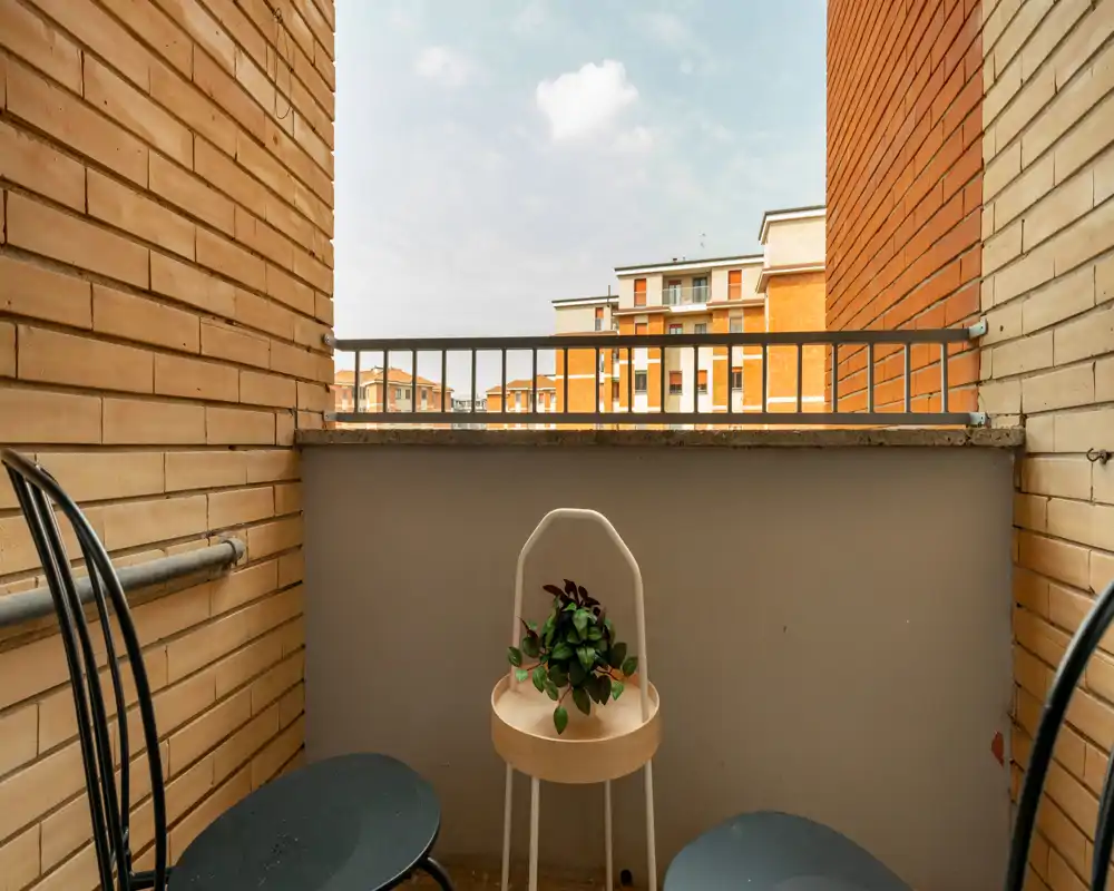 Petit balcon cosy avec deux chaises et une plante, murs en brique et vue sur les immeubles voisins — idéal pour un café du matin.