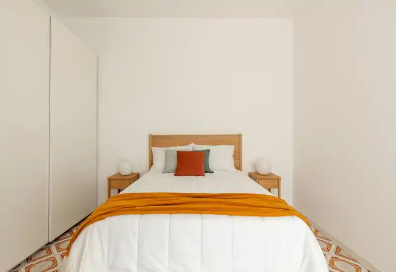 Chambre double lumineuse et minimaliste avec tête de lit en bois, tables de chevet et accents textiles chauds comme un plaid orange et des coussins décoratifs.