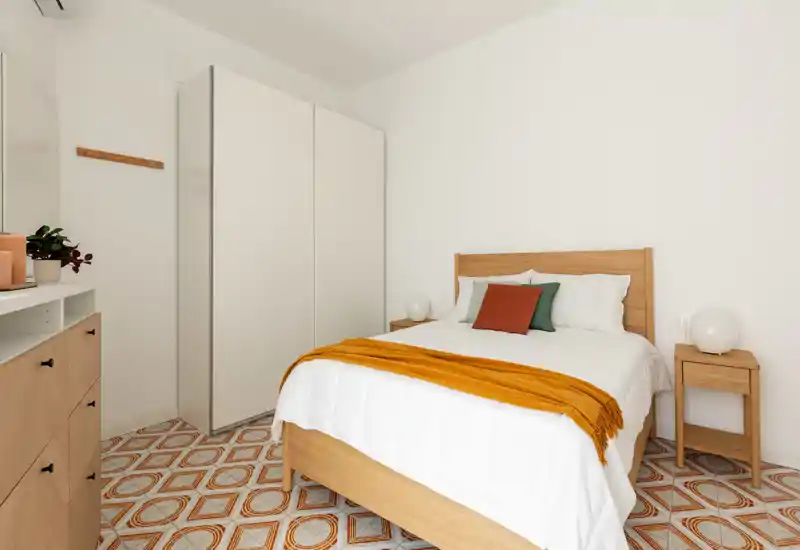 Chambre lumineuse et minimaliste avec lit en bois, coussins confortables et plaid moutarde, armoire et tables de chevet — idéale pour un séjour agréable.