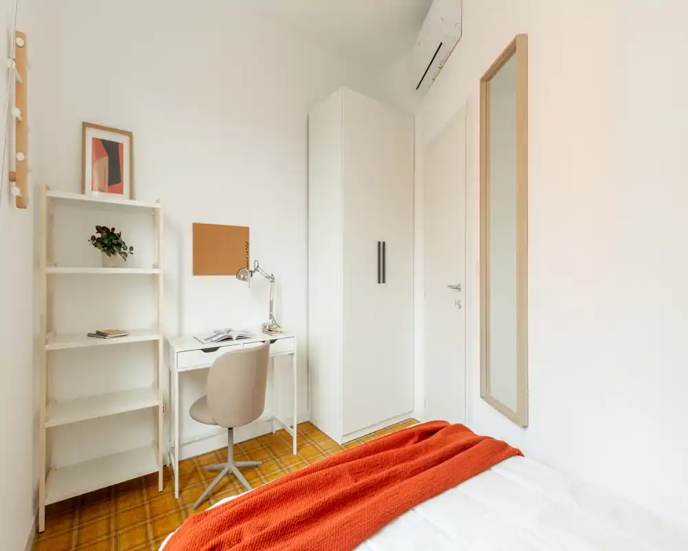 Petite chambre lumineuse avec bureau blanc, armoire et lit habillé d'un plaid orange chaleureux ; décoration minimale et moderne, belle luminosité — parfaite pour une personne ou un étudiant.