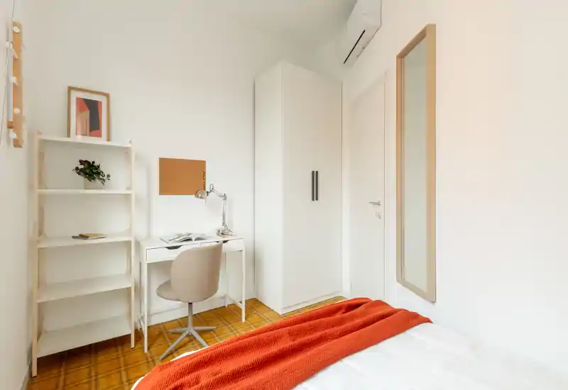 Petite chambre lumineuse avec bureau blanc, armoire et lit habillé d'un plaid orange chaleureux ; décoration minimale et moderne, belle luminosité — parfaite pour une personne ou un étudiant.