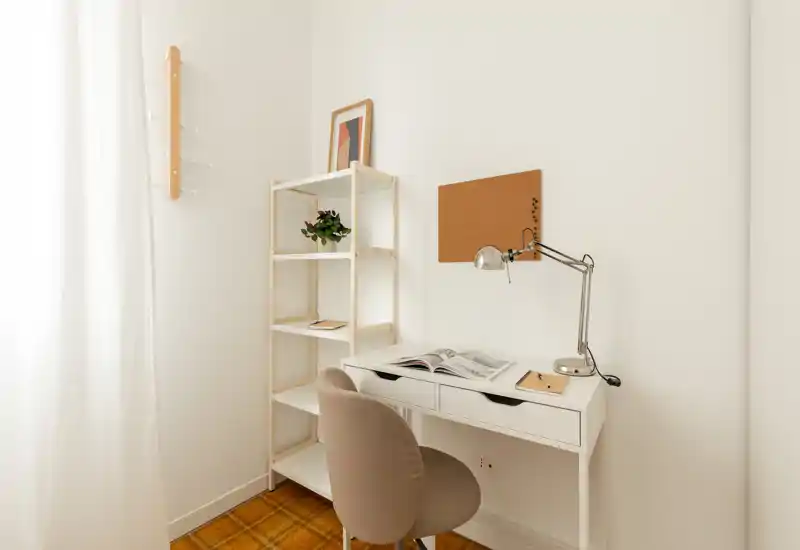 Coin bureau lumineux et minimaliste avec bureau blanc, lampe chromée réglable, étagère et chaise rembourrée confortable — idéal pour télétravailler ou étudier.
