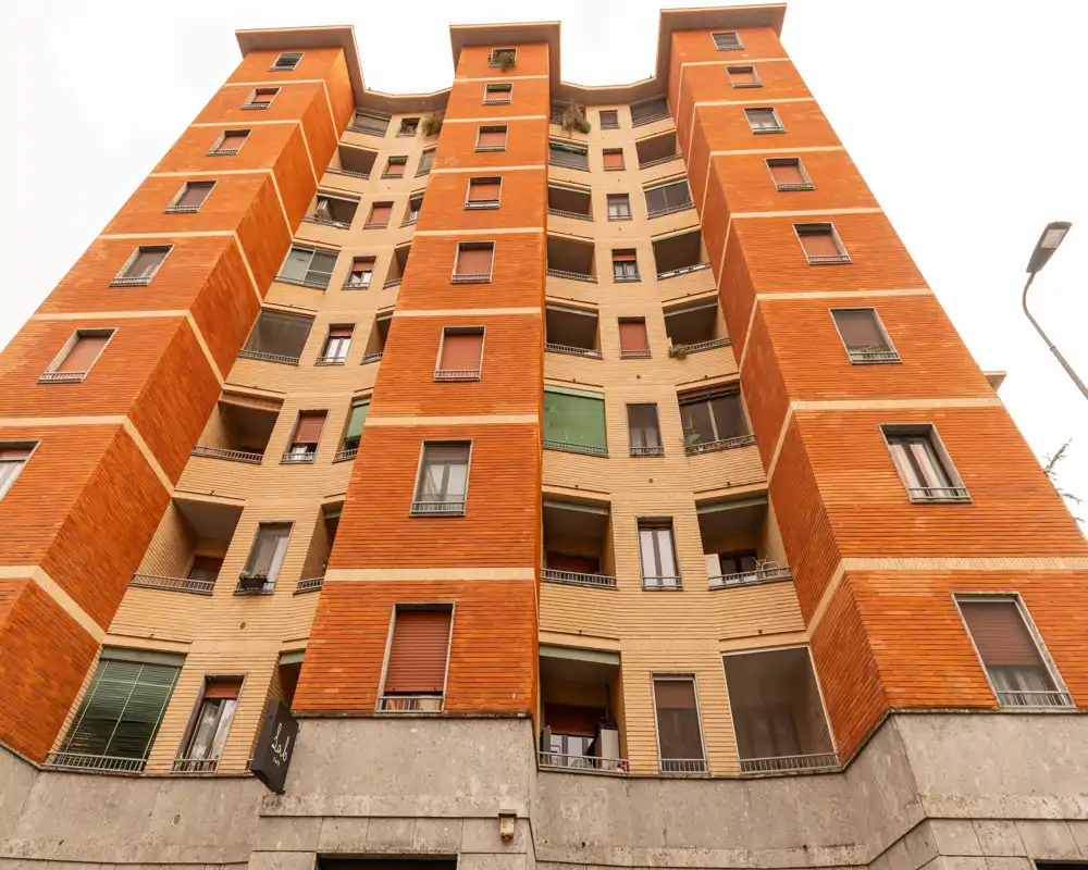 Vue extérieure d'un immeuble résidentiel de plusieurs étages avec sections verticales en briques rouges et balcons, pris au niveau de la rue en perspective ascendante.