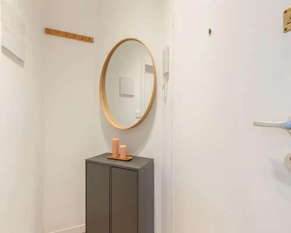 Entrée compacte et minimaliste avec miroir rond, petit meuble console et bougies décoratives — lumineuse, propre et accueillante.