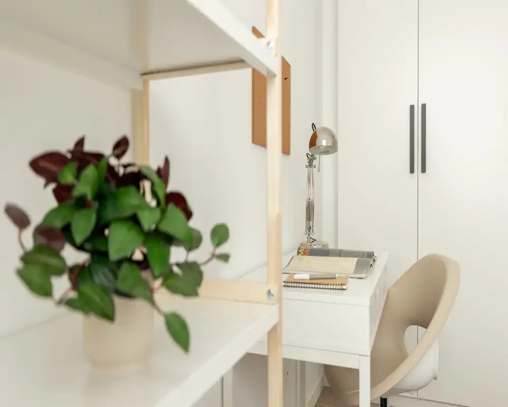 Angolo studio luminoso e minimale con scrivania bianca, sedia beige e pianta decorativa, ideale per un piccolo ufficio domestico.