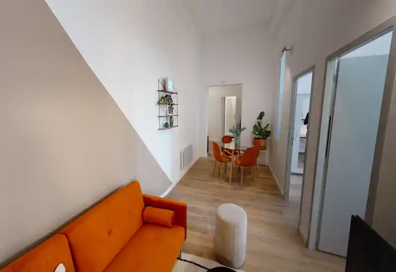 Salon moderne et lumineux avec un canapé orange vif, une table à manger ronde et une déco soignée; parquet et plantes pour une ambiance chaleureuse.