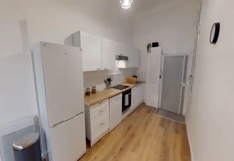 Cuisine compacte et moderne avec placards blancs, plan de travail en bois, four et lave-vaisselle intégrés. Agencement lumineux et propre, parfait pour la location.