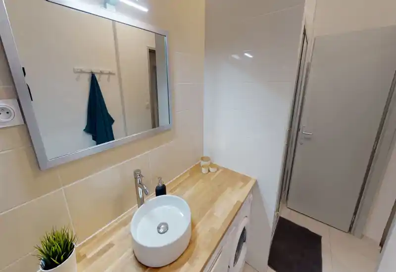 Salle de bain moderne avec vasque ronde sur plan de travail en bois, miroir éclairé, murs carrelés et lave-linge intégré sous le plan.