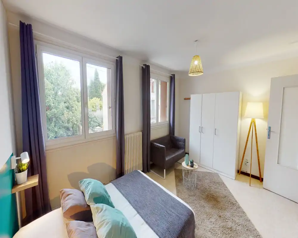 Bright, well-styled bedroom with a comfortable double bed, large windows overlooking greenery, a small seating area and a freestanding wardrobe — ideal for a relaxing stay.