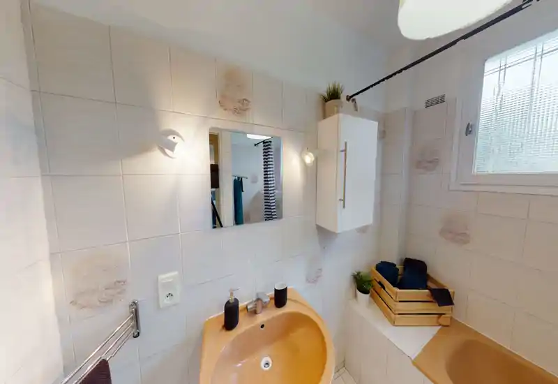 Salle de bains lumineuse et soignée avec carrelage, lavabo et baignoire couleur pêche, miroir mural et armoire de rangement — idéale pour un séjour confortable.