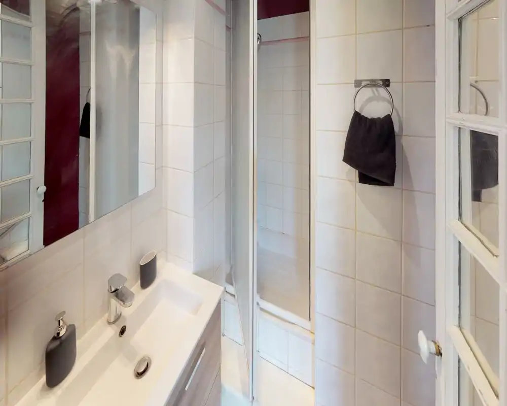 Clean, compact bathroom with a white tiled interior, sink with modern fixtures, mirrored cabinet and a small shower cubicle.