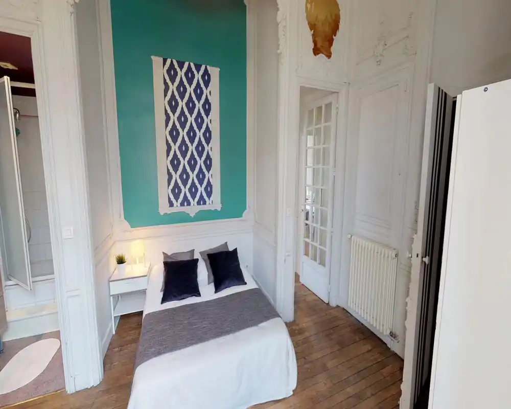 Bright, stylish bedroom with a double bed, decorative pillows and a bedside table with lamp; classic moulding and a teal accent wall add character.