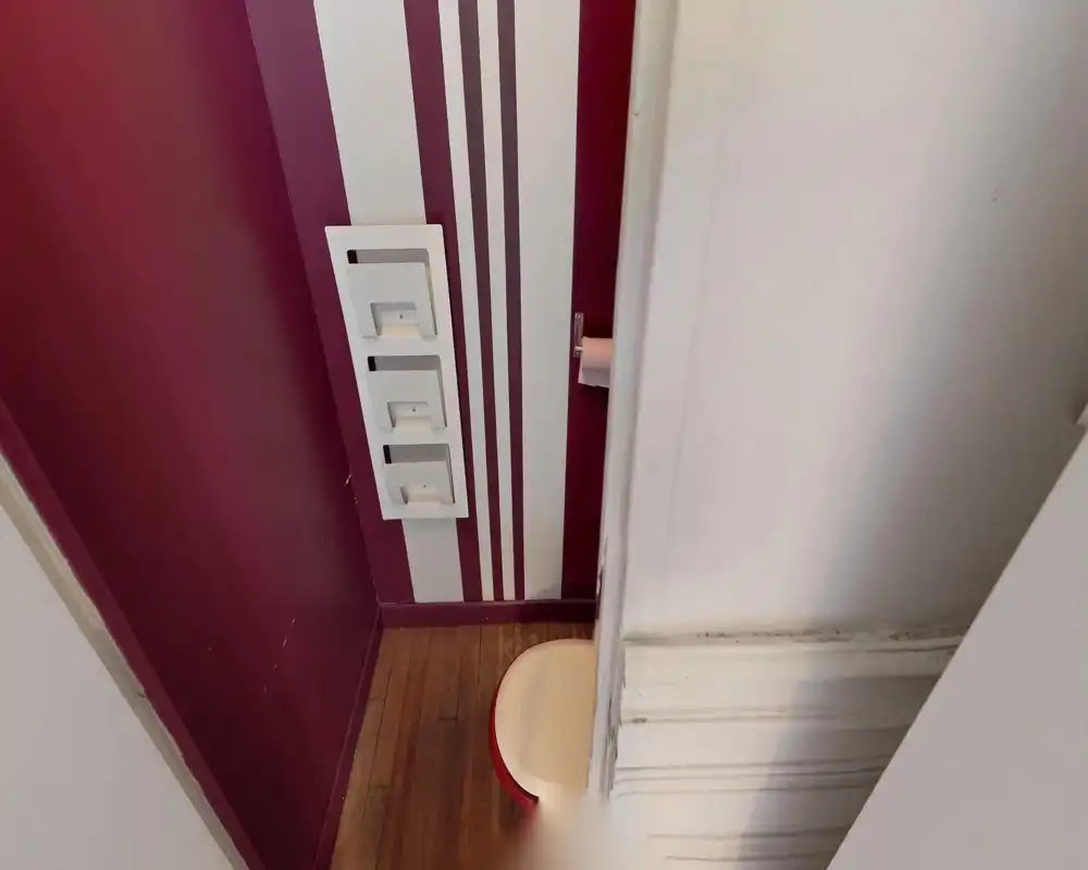 Compact bathroom corner with a visible toilet seat and toilet-paper holder, wooden floor and decorative vertical stripes on the wall. The photo highlights a small, well-decorated WC area.