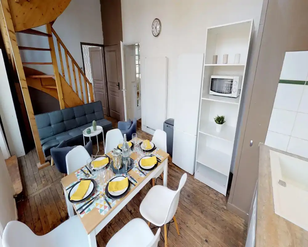 Spacious and stylish living/dining area with a wooden spiral staircase, comfortable sofa and a table set for six — warm wooden floors and modern decor create a welcoming communal space.