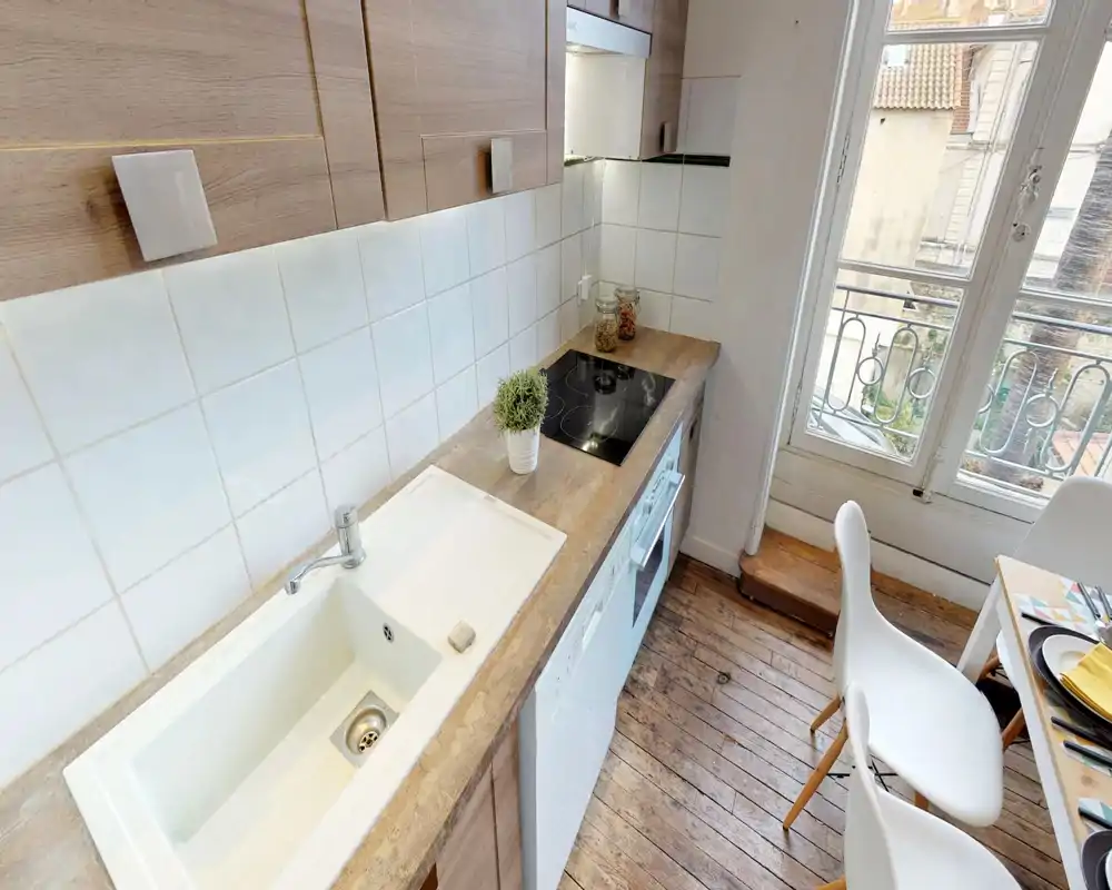 Compact modern kitchen with a wooden countertop, built-in induction hob, sink and a bright window overlooking a small balcony. The warm wooden floor and simple decor create a welcoming cooking and dining corner.