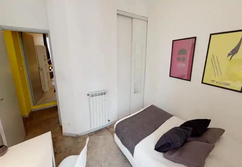 Chambre moderne et lumineuse avec lit bien fait, coussins décoratifs, plaid texturé et affiches encadrées — un espace compact et chaleureux parfait pour des courts séjours.