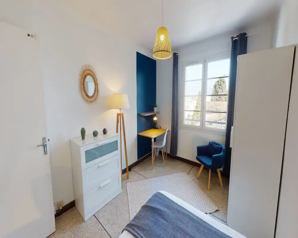 Camera da letto luminosa e ben allestita con letto visibile in primo piano, una scrivania vicino alla finestra e una poltroncina accogliente — ideale per una persona o uno studente.