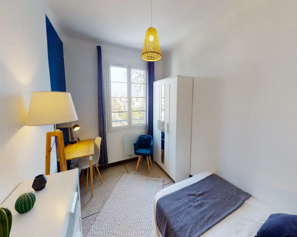 Camera da letto luminosa e ben arredata con letto rifatto, armadio con specchio e una scrivania vicino alla finestra — perfetta per un soggiorno confortevole.
