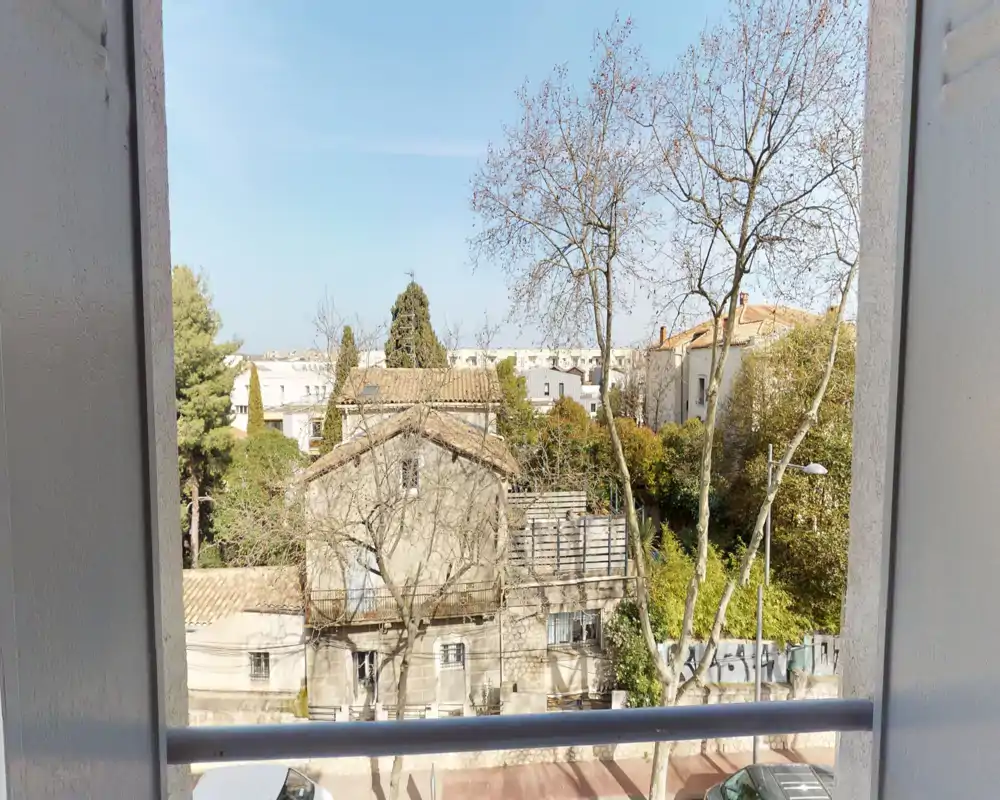 Vue depuis le balcon ensoleillé sur des maisons et des arbres, ciel bleu clair et rue en contrebas.