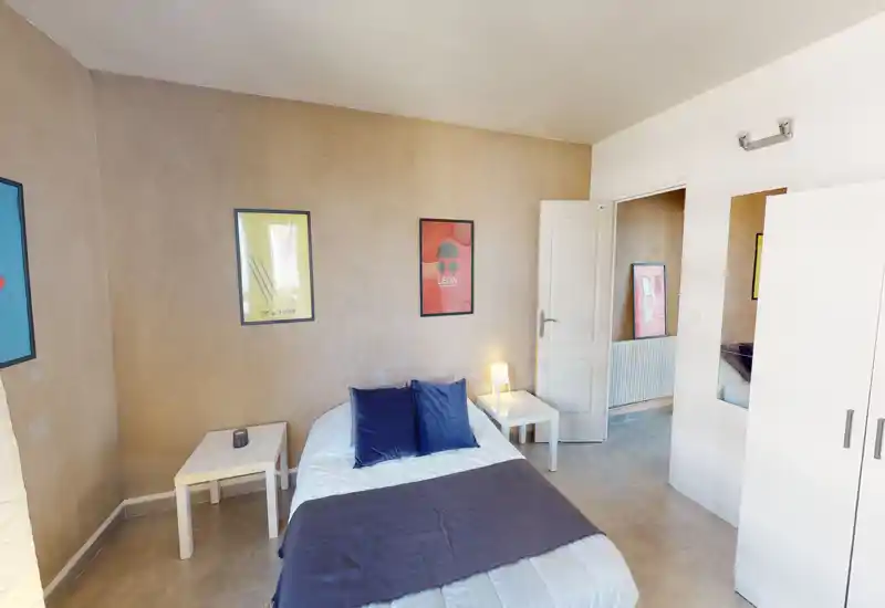 Chambre lumineuse et bien décorée avec un lit double soigné, tables de chevet, coussins et tableaux muraux — espace propre et accueillant.
