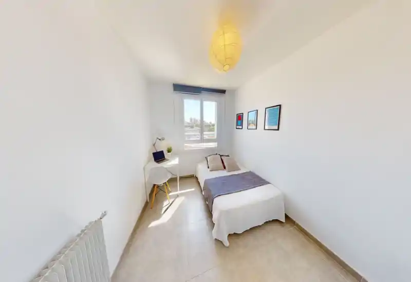 Chambre simple lumineuse et compacte avec lit bien fait, petit bureau près de la fenêtre et lumière naturelle — idéale pour étudiant ou une personne seule.
