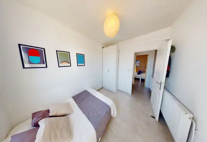 Chambre simple lumineuse et soignée avec lit au premier plan, linge doux, tableaux muraux et placard intégré; palette neutre idéale pour les annonces locatives.
