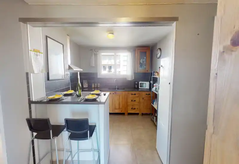 Cuisine compacte et lumineuse avec coin bar, deux tabourets et meubles en bois. Idéale pour des repas conviviaux et une cuisine fonctionnelle, bien éclairée.