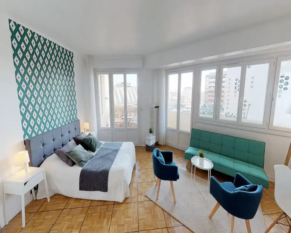 Chambre/studio spacieuse et lumineuse avec lit double confortable, mur d'accent à motif et coin salon avec canapé et fauteuils — parfaite pour un séjour urbain élégant et ensoleillé.