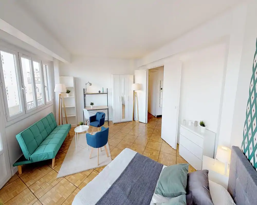 Chambre spacieuse et lumineuse avec un lit confortable au premier plan, des textiles soignés et un coin salon avec canapé et fauteuils. Grandes fenêtres apportant beaucoup de lumière naturelle, mise en scène propre et accueillante.