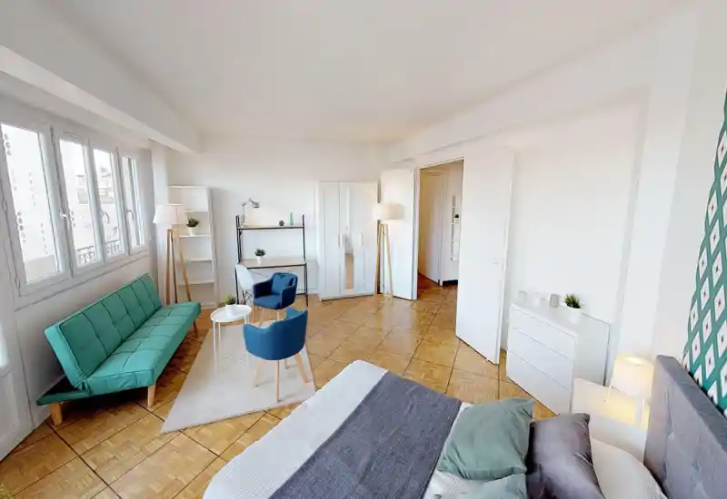 Chambre spacieuse et lumineuse avec un lit confortable au premier plan, des textiles soignés et un coin salon avec canapé et fauteuils. Grandes fenêtres apportant beaucoup de lumière naturelle, mise en scène propre et accueillante.