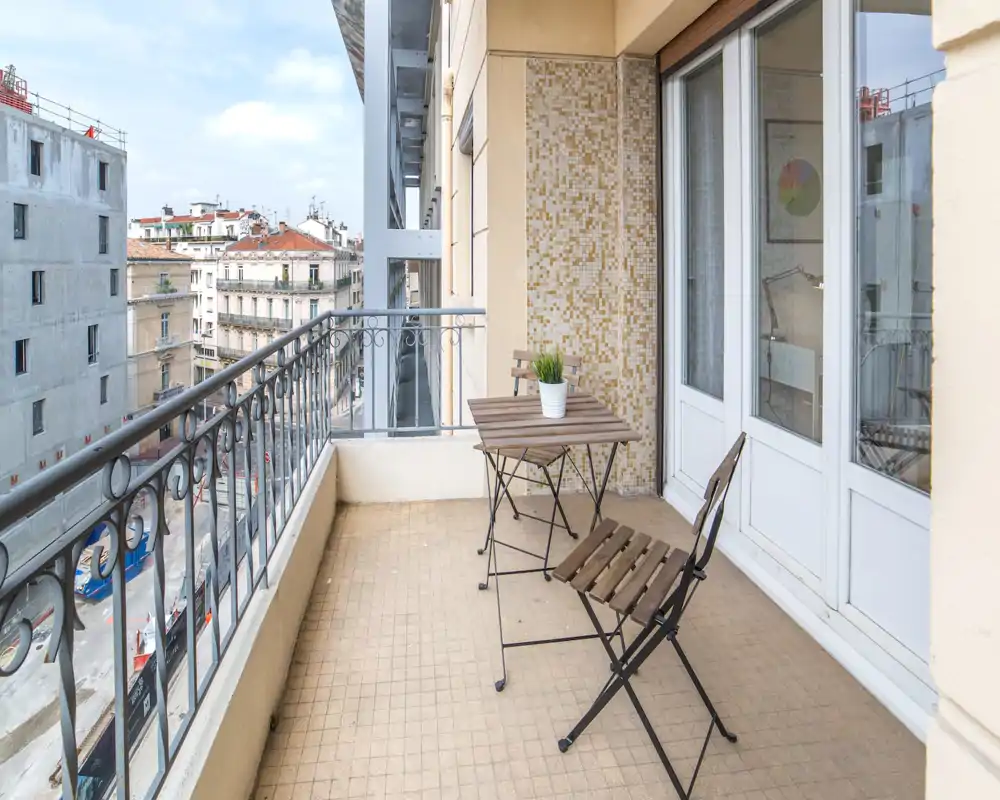 Balcone soleggiato con un piccolo tavolo in legno e due sedie pieghevoli che si affacciano sulla città — ideale per un caffè al mattino.
