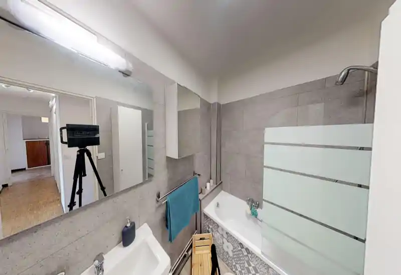 Salle de bain moderne avec baignoire et pare-douche, meuble mural, lavabo et miroir ; carrelage gris neutre et panneau décoratif pour un look propre et contemporain.