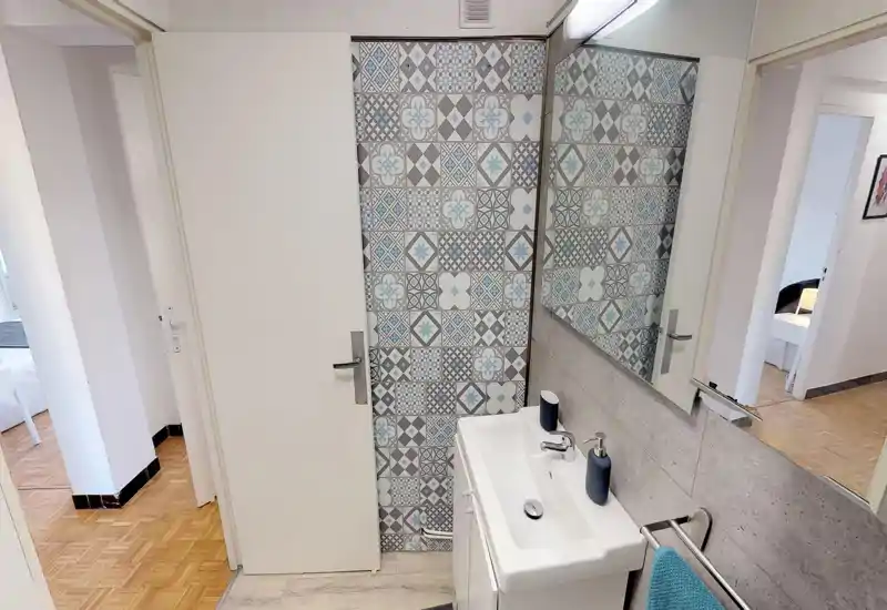 Petite salle de bain moderne avec carrelage décoratif à motifs, lavabo blanc et robinet chromé, grand miroir et finitions neutres propres — lumineux et soigné.