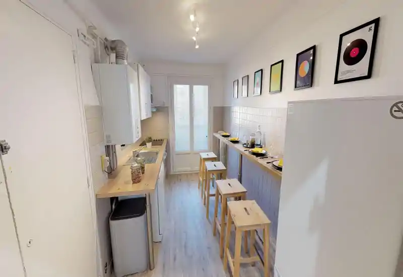 Cuisine étroite et bien aménagée avec plan de travail en bois, évier et plaque compacts, et un bar avec tabourets. Lumineuse et soignée, parfaite pour un petit appartement urbain.