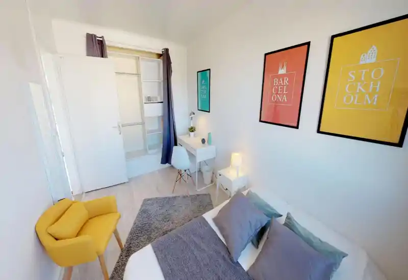 Bright, well-staged bedroom with a comfortable-looking bed, bedside table and desk. Colorful framed prints and coordinated textiles create a modern, inviting atmosphere ideal for listings.