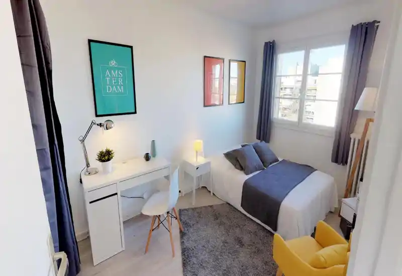 Sunny, modern bedroom with a double bed, bedside table and a small desk. Neutral décor, soft textiles and large window create a bright, comfortable space ideal for short stays.