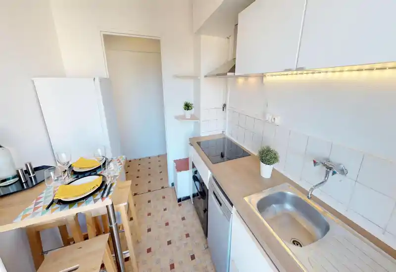 Compact staged kitchen with a sink, induction hob, dishwasher and a small breakfast bar set for two — bright, tidy and practical for a city apartment.