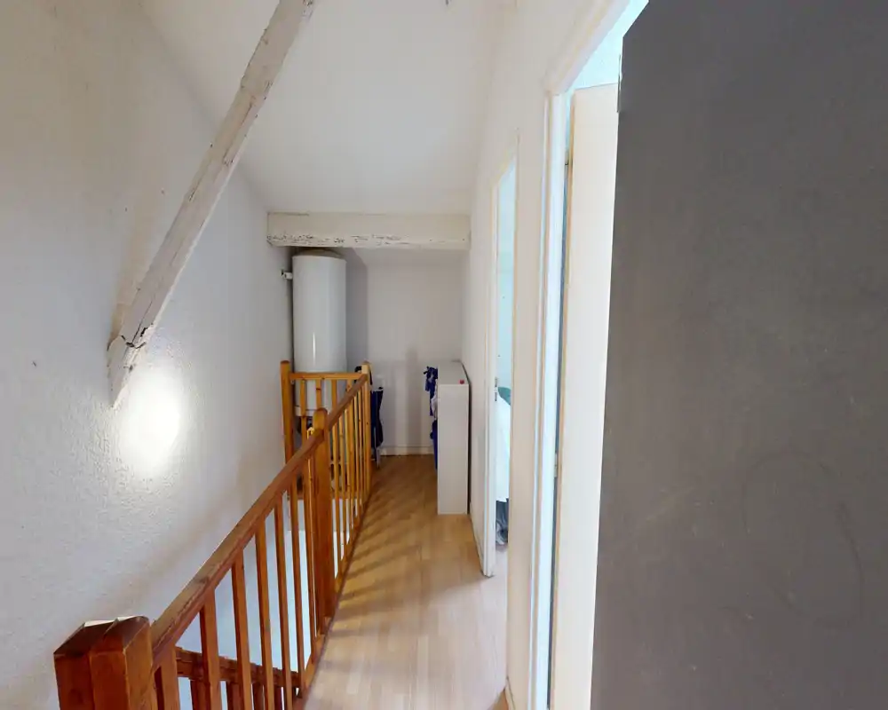 Narrow upstairs landing with wooden railing, laminate flooring and a hot-water cylinder at the far end; bright, simple circulation space connecting rooms.