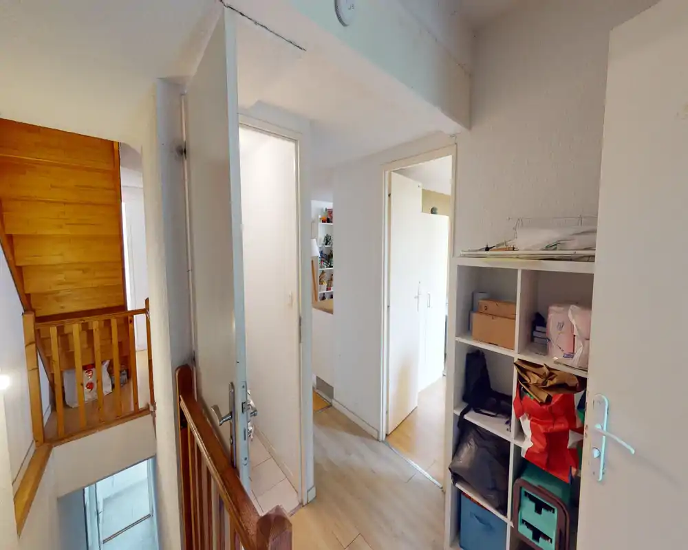 Bright landing/entrance area with wooden stair railing, open doors leading to adjacent rooms and shelving for storage — a practical transitional space with natural light.
