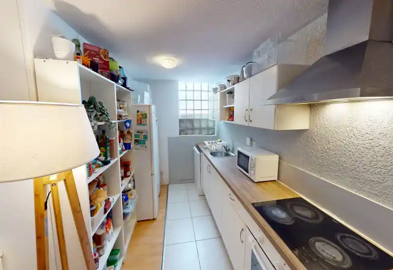 Cuisine en longueur bien organisée avec placards blancs, plan de travail effet bois, plaque de cuisson intégrée et micro-ondes ; espace lumineux et pratique pour la vie quotidienne.